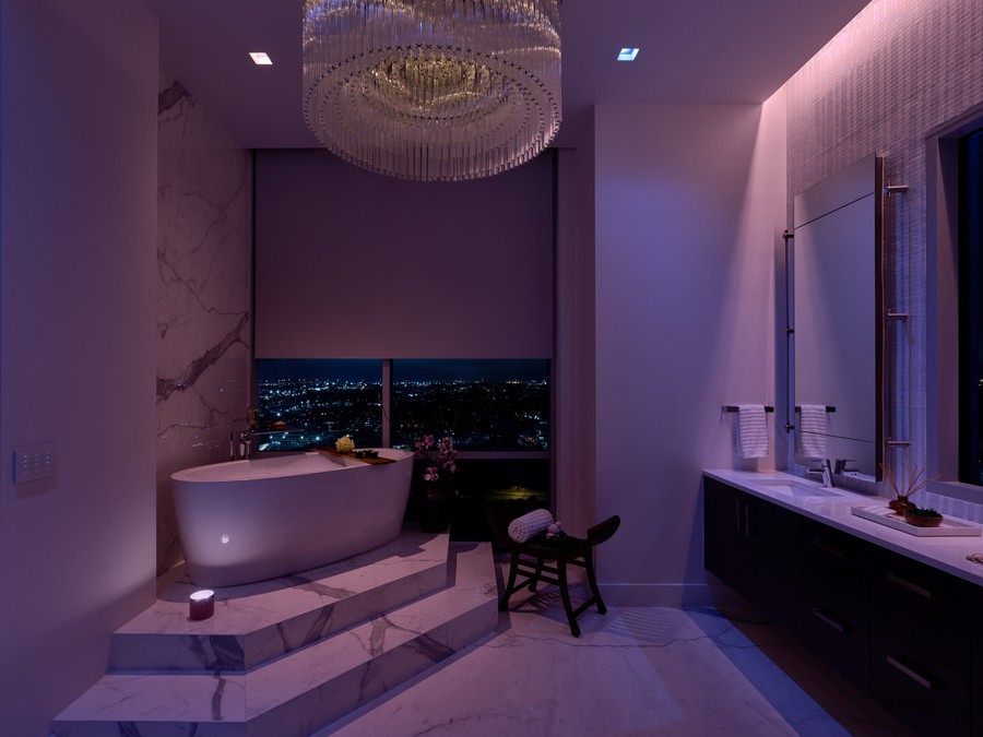 A bathroom with a soaking tub and half-drawn shades illuminated in a violet light.