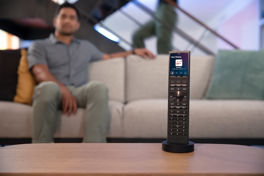 A Control4 remote rests on a table as a man enjoys home entertainment.